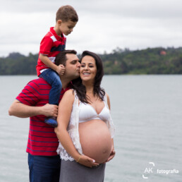 pai com o filho nos ombros beijando o rosto da esposa grávida