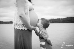 foto P&B do filho beijando a barriga da mãe gestante em ensaio fotográfico