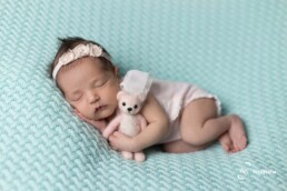 foto bebê recém nascido deitado de lado segurando um ursinho