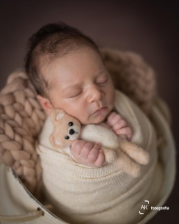 foto newborn bebe enrolado no wrap segurando ursinho