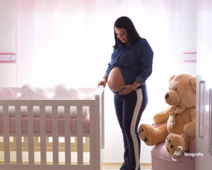 gestante olhando para a barriga ao lado do berço do bebê