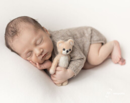 newborn deitado de lado segurando um ursinho