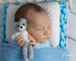 bebê recem nascido segurando um ursinho cinza